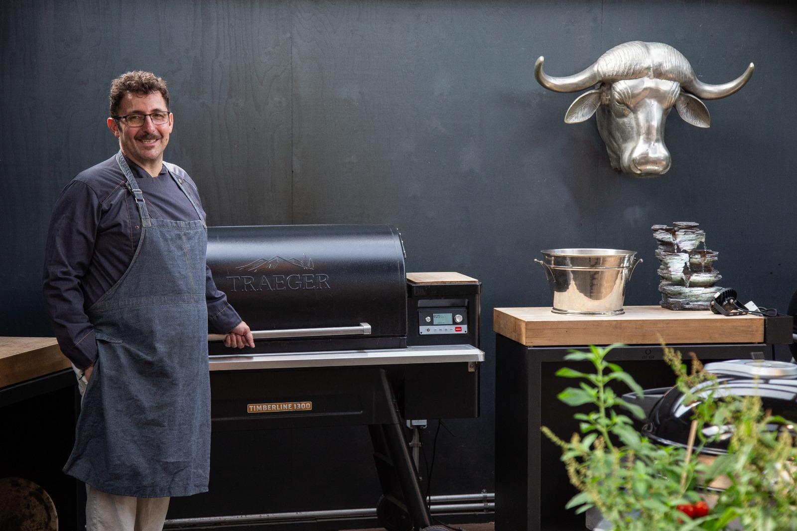 Hermann Donnik im BBQ Raum Hürth am Smoker mit Schürze, lächelnd in die Kamera – rechts im Bild der dekorative Stierkopf als markantes Detail