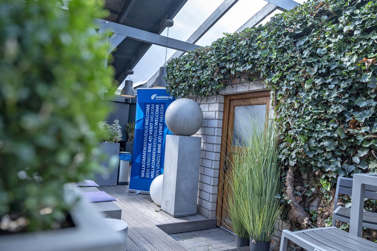 Blick auf die Terrasse des BBQ Raum Hürth mit Efeu bewachsener Wand – stilvolle Outdoorfläche für Events