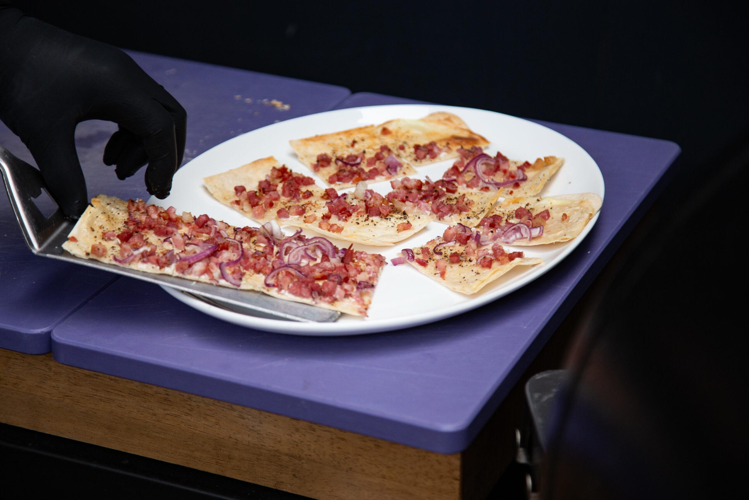 Frisch gebackener Flammkuchen wird im BBQ Raum Hürth geschnitten und an die Gäste verteilt – direkt vom Holzbrett auf die Teller